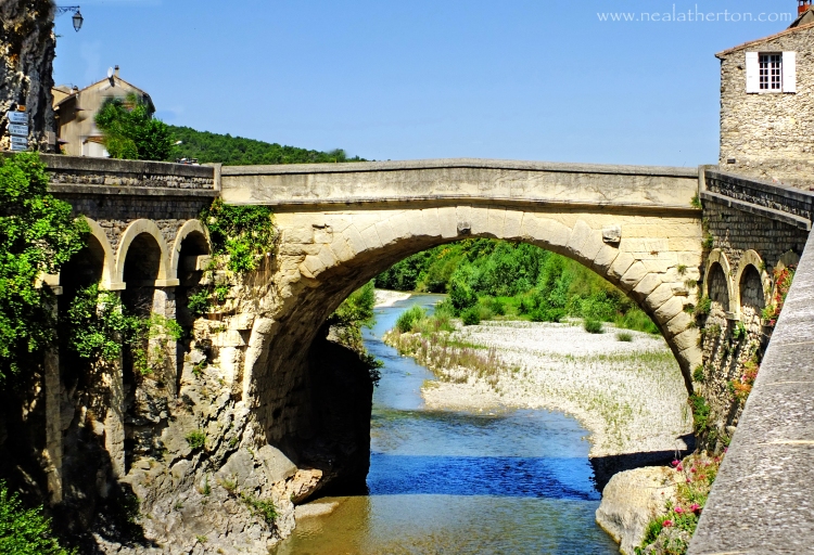Looking down the river under the old Roman bridge to the old town of Vaison La Romaine in Provence France in French Travel guide book